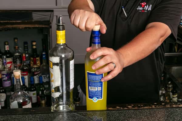 Bartender opening a bottle of limoncello behind a fully stocked bar, preparing for cocktail service.