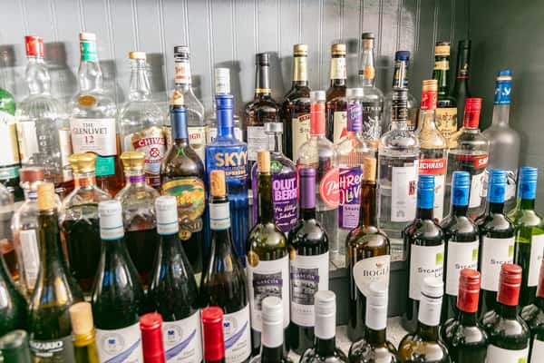 Fully stocked bar with a wide selection of liquor and wine bottles, including vodka, whiskey, rum, and red and white wines, arranged against a gray panel backdrop.
