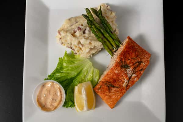 Grilled salmon fillet served with garlic mashed potatoes, roasted asparagus, lemon wedge, and creamy sauce on a white plate