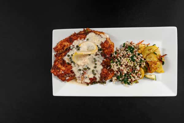 Pan-seared chicken piccata topped with lemon slices and caper cream sauce, served with wild rice pilaf and sautéed squash on a rectangular white plate.