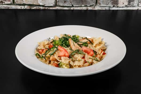Bowtie pasta with grilled chicken, diced tomatoes, and broccoli in a creamy garlic sauce, garnished with fresh basil.