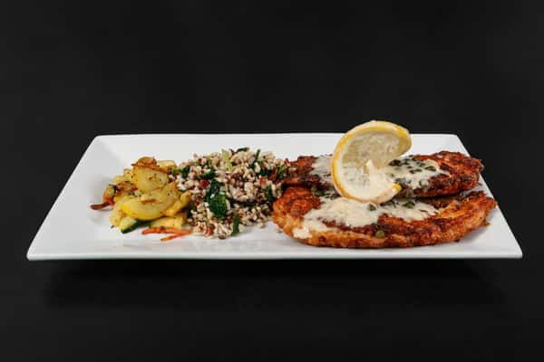 Pan-fried chicken piccata with lemon caper sauce, served with wild rice pilaf and sautéed squash on a rectangular plate.