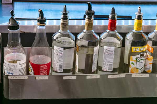 Assorted labeled liquor bottles arranged in a bar well, including vodka, whiskey, and citrus liqueur.