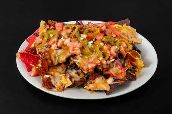 Loaded nachos with melted cheese, tomatoes, jalapeños, and chili on colorful tortilla chips, served on a white plate.