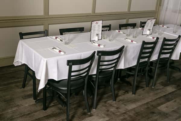 Elegant private dining setup with black chairs, white tablecloths, neatly rolled napkins, and printed menus on a hardwood floor.