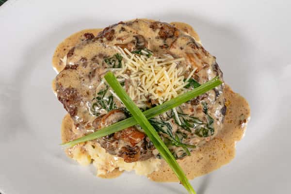 Ground beef steak smothered in creamy mushroom sauce, topped with shredded Parmesan and green onions, served over mashed potatoes.