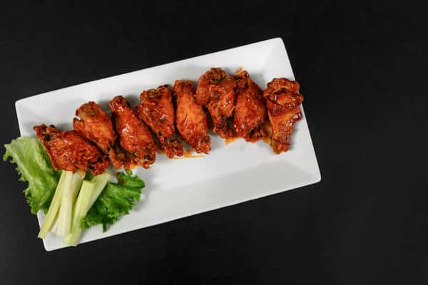 Plated buffalo chicken wings coated in spicy sauce, served with celery sticks and romaine on a white rectangular plate.