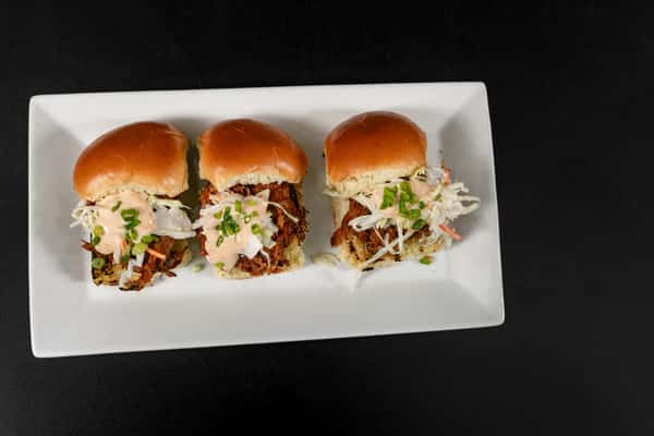 Three pulled pork sliders topped with creamy coleslaw and chopped chives, served on soft brioche buns.