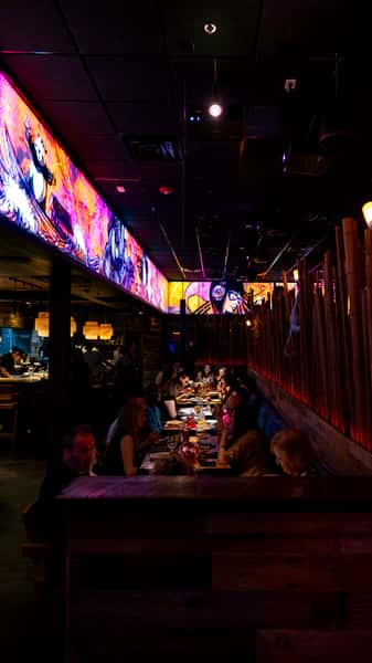 Guests dining beneath illuminated artwork at Kapow! Noodle Bar, enjoying premium Asian fusion cuisine in a vibrant, high-energy nightlife atmosphere.