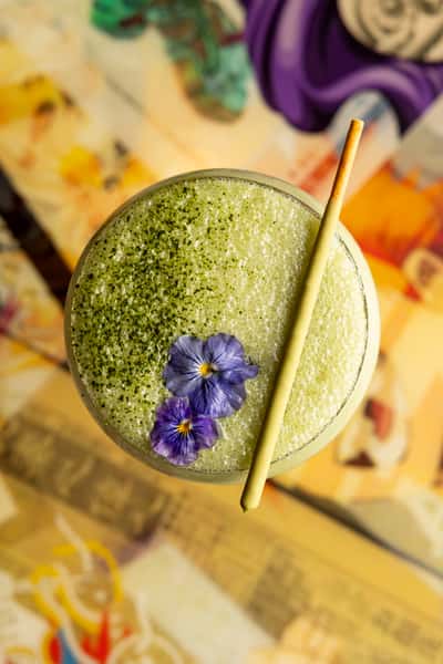 Green cocktail topped with a frothy herb-infused foam and garnished with an edible flower at Atlantic Current restaurant
