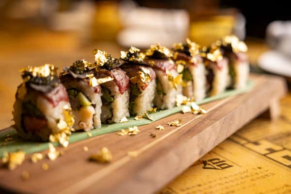 Specialty sushi roll topped with gold flakes on a wooden board at Kapow! Noodle Bar, featuring fresh sushi and elevated Asian fusion cuisine