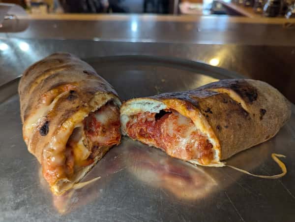 Cheesy pepperoni calzone sliced open to reveal melted cheese and marinara sauce on a metal tray.