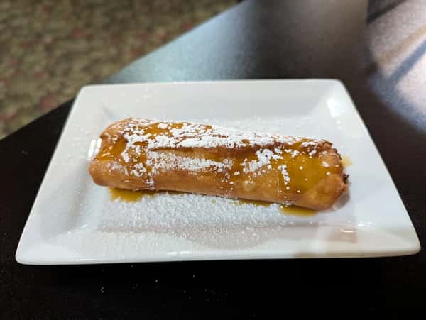 Fried dessert pastry topped with powdered sugar and drizzled with syrup on a white square plate.