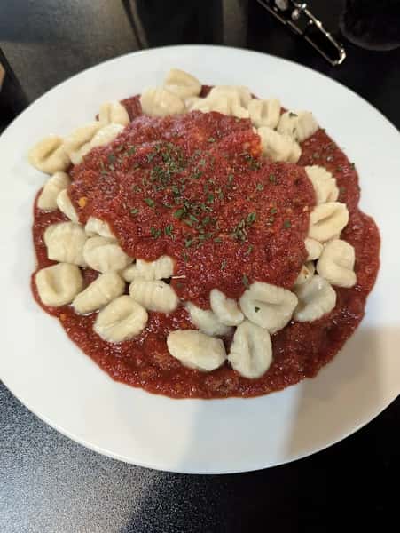 Plate of gnocchi topped with marinara sauce and garnished with herbs.
