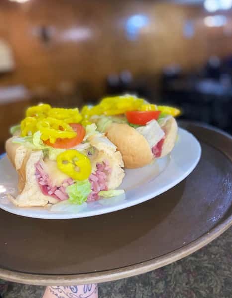 Italian sub sandwich filled with deli meats, melted cheese, lettuce, tomato, and banana peppers on a white plate.
