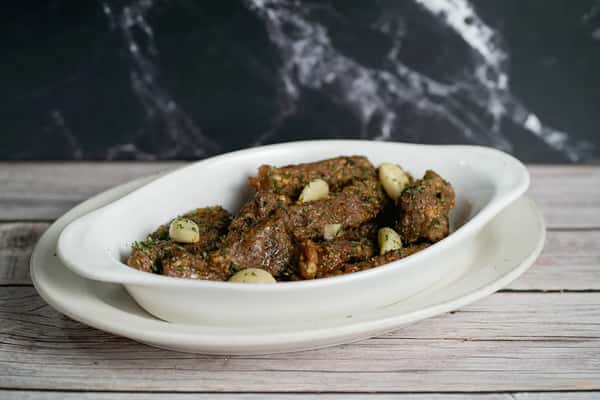 Seasoned Italian sausage pieces garnished with garlic cloves and herbs, served in a white oval dish.