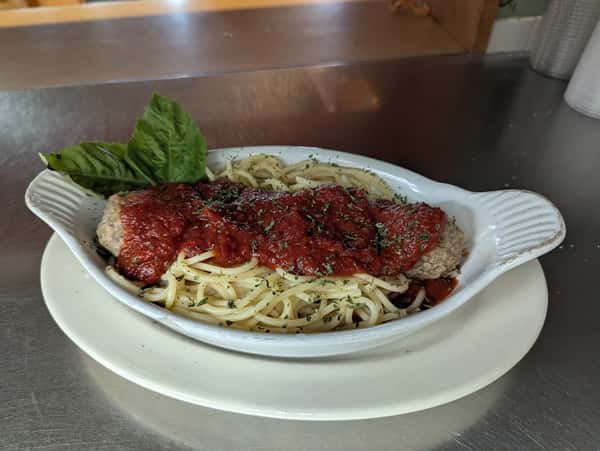 Spaghetti with marinara sauce and a large meatball, garnished with herbs and fresh basil, served in a white oval dish.