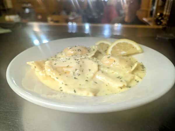 Cheese ravioli in a creamy alfredo sauce garnished with herbs and lemon wedges, served on a white plate.