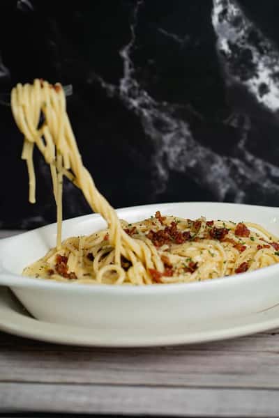 Spaghetti carbonara topped with crispy bacon bits and herbs, twirled on a fork, served in a white oval dish.