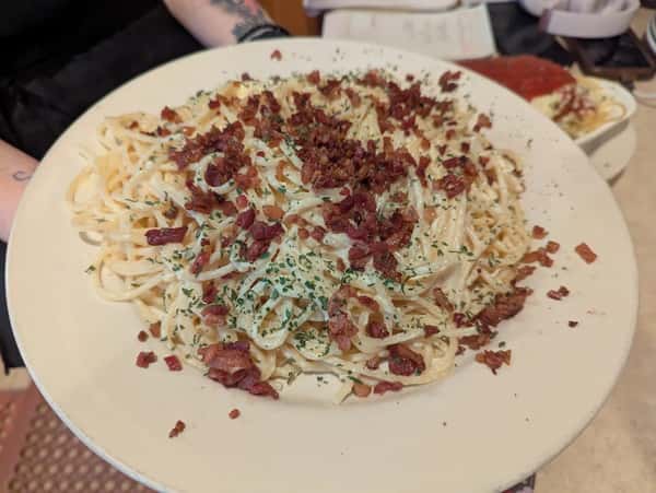 Large plate of creamy fettuccine pasta topped with crispy bacon bits and chopped herbs.