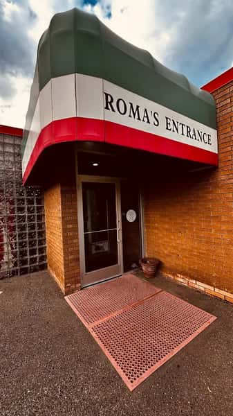 Restaurant entrance with a red, white, and green awning labeled "ROMA'S ENTRANCE" above a glass door and red floor mat.