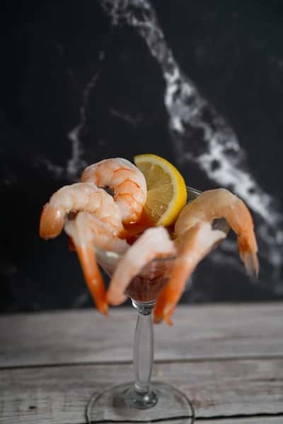 Shrimp cocktail served in a glass with cocktail sauce and a lemon wedge on a rustic wooden surface.