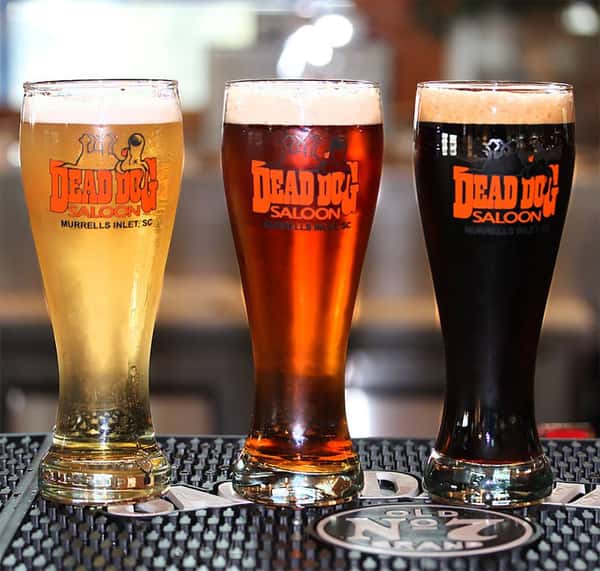 Three beers in long glasses with Dead Dog Saloon logo on them