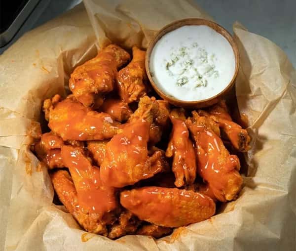 Basket of buffalo chicken wings coated in hot sauce, served with a side of chunky blue cheese dressing.