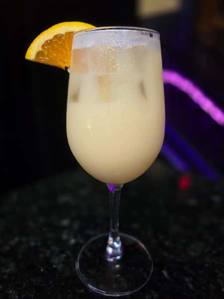 Creamy orange cocktail served over ice in a wine glass, garnished with a fresh orange slice, on a dark marble surface.