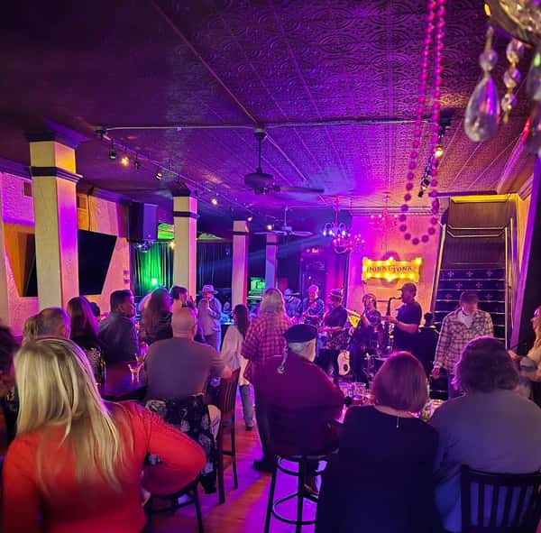 Crowd enjoying live music performance in a dimly lit venue with purple lighting and "HONKY TONKIC" sign on the stage.