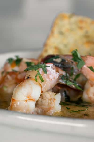 Close-up of garlic butter shrimp garnished with fresh parsley and served with toasted bread, a classic Italian seafood appetizer in a rich white wine sauce.