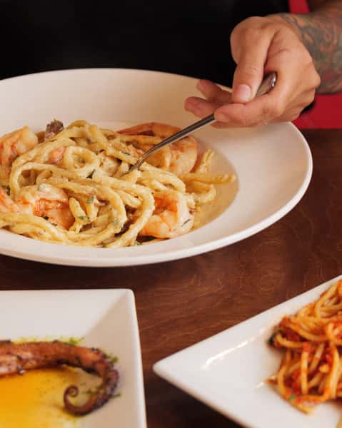 Creamy shrimp linguine served in a white bowl with herbs and garlic sauce, photographed on a rustic wooden restaurant table.