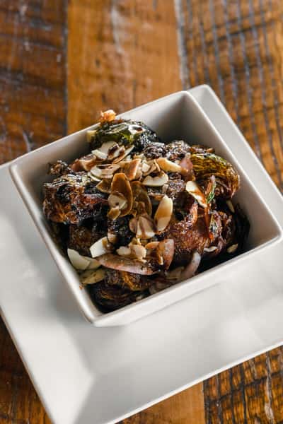 Roasted vegetables with toasted almonds and caramelized onions in a white bowl, a rustic Italian vegetable side dish.