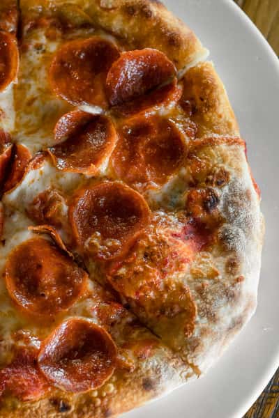 Close-up of a wood-fired pepperoni pizza with crispy curled pepperoni and melted mozzarella on a blistered Neapolitan-style crust.
