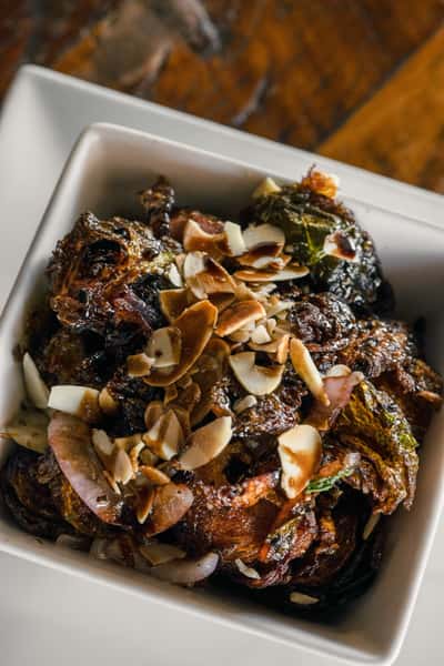 Roasted Italian vegetables with caramelized onions and toasted almonds served in a white bowl, a rustic Mediterranean-style side dish.