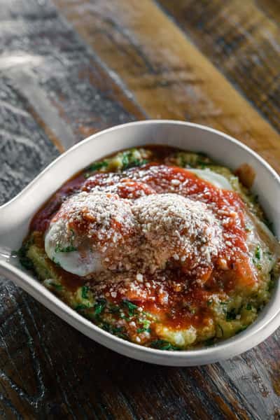 Baked Italian meatballs topped with marinara sauce, melted mozzarella, and grated parmesan served in a small casserole dish.