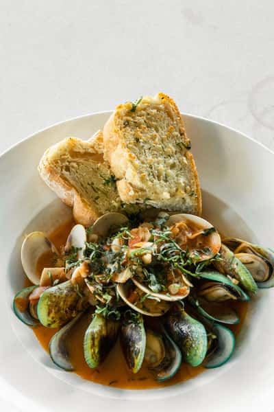 Steamed mussels in a rich tomato broth topped with fresh herbs and served with garlic bread at an Italian restaurant.