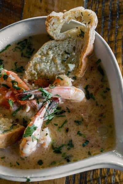 Shrimp scampi in a garlic butter and white wine sauce topped with chopped herbs and served with toasted bread at an Italian restaurant.