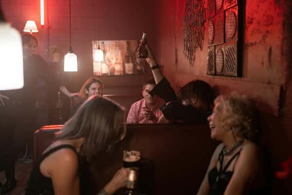 People socialising in a dim bar with red lighting, some holding drinks.