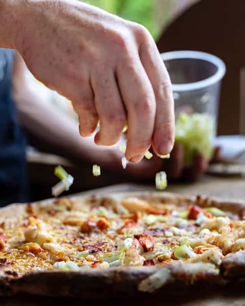 Toppings being sprinkled on a pizza