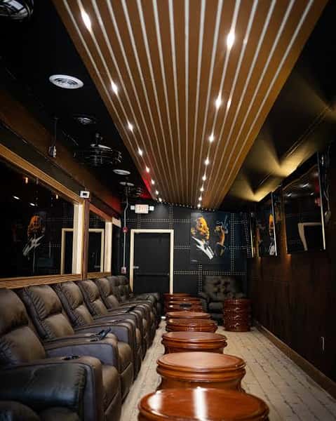 Sleek cigar lounge interior with black leather recliners, round wooden tables, and ambient ceiling lighting, featuring jazz-themed wall art for a sophisticated, modern vibe.