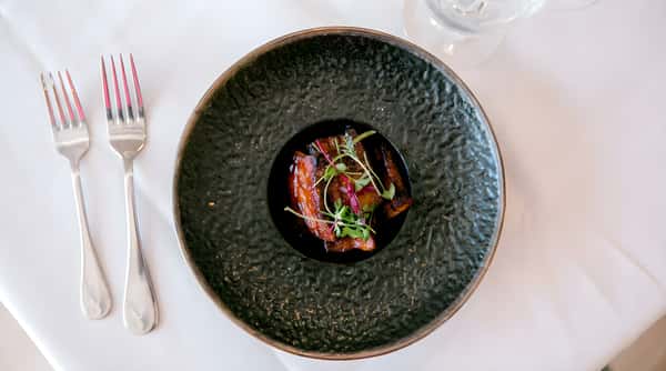 Fine dining plate with pork belly and microgreens in a black bowl.