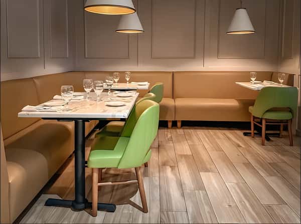 Modern restaurant dining room with booth seating, green chairs, and set tables.