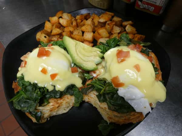 Vegetarian eggs Benedict with sautéed spinach, tomato, avocado, and hollandaise on toasted bread, served with seasoned breakfast potatoes.