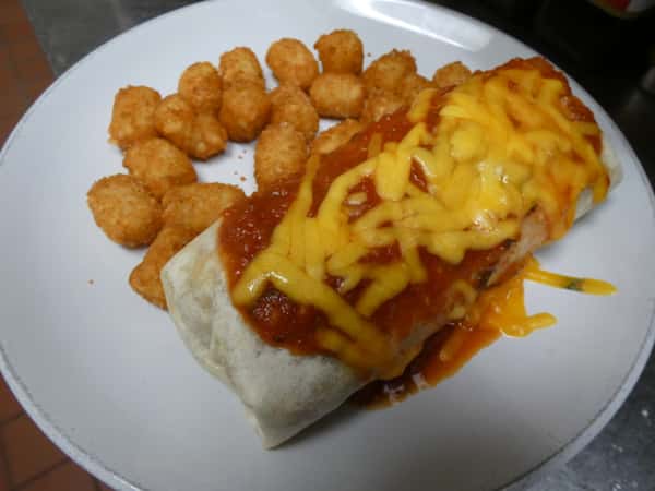 Smothered breakfast burrito topped with red salsa and melted cheddar cheese, served with a side of crispy golden tater tots.