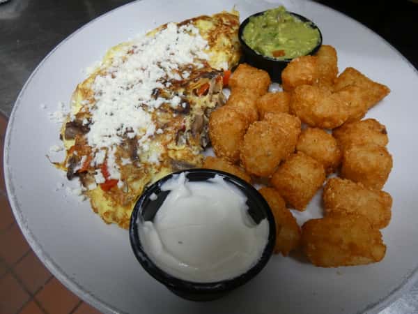 Southwest-style omelette with mushrooms, peppers, and crumbled cheese, served with tater tots, guacamole, and a side of sour cream.