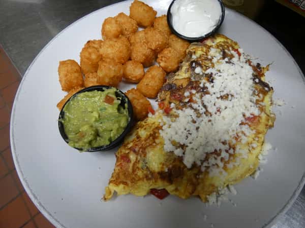 Southwest omelette topped with crumbled cheese, served with crispy tater tots, guacamole, and a side of sour cream.