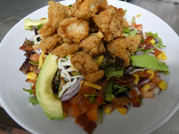 Crispy fried chicken salad with avocado, shredded cheese, corn, bacon, red onion, and diced tomato over a bed of mixed greens.