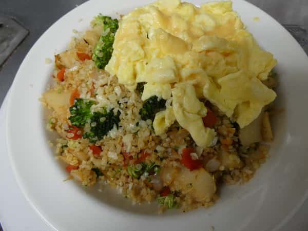 Scrambled eggs served over a hearty vegetable fried rice with broccoli, bell peppers, onions, and diced potatoes in a white bowl.