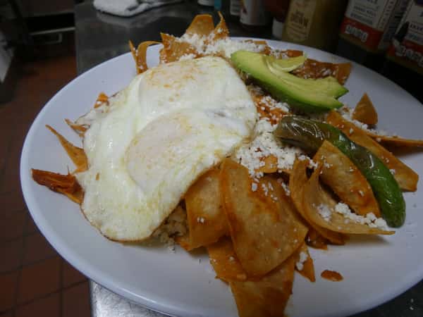 Chilaquiles rojos with crispy tortilla chips in red sauce, topped with fried eggs, avocado slices, jalapeños, and crumbled queso fresco.